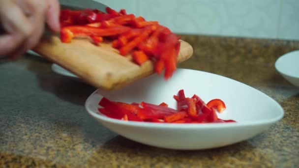 Hand einer Frau fügt rotes Paprika zu einem Teller auf einem Holzbrett hinzu — Stockvideo