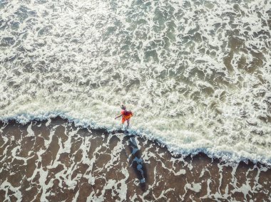 Deniz kıyısında duran genç bir sarışının hava aracı, bacaklarını dalgalarla kaplıyor. Sıcak plaj, serin dalgalar. Yaz ve rahatlama kavramı, bir kızla deniz manzarası, plaj, güzel dalgalar.