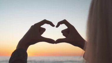 Güzel kız elleriyle denizin arka planında kalp yapıyor..