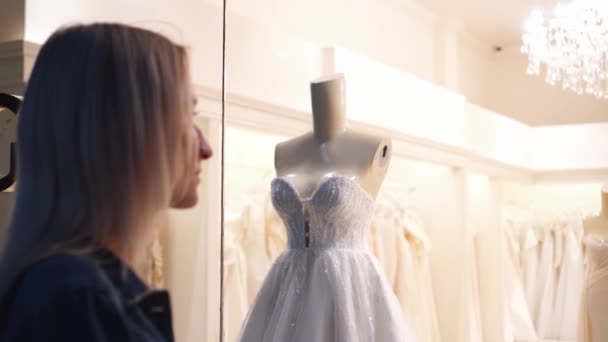 Meisje benadert venster van bruiloft winkel en kijkt naar mooie trouwjurken — Stockvideo