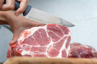 Kadın eli, bıçakla yakın plan kesim. Kesme tahtasında büyük bir parça taze domuz eti, kopyalama alanı.