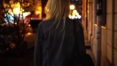 Kot ceketli, şehir merkezinde yürüyen şık bir kadının arka görüntüsü.
