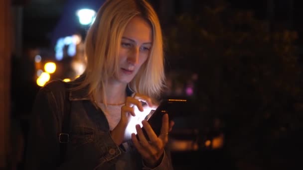 Kot ceketli bir sarışın akıllı telefonuna bakarak şehirde dolaşıyor. — Stok video