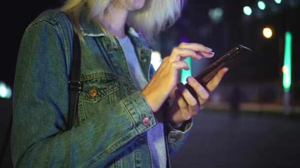 Žena používá smartphone ke komunikaci v nočním městě. na pozadí mrakodrapů — Stock video