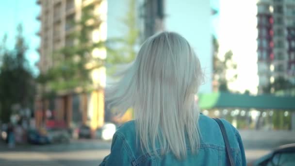 Vista trasera de la joven rubia con estilo en chaqueta de mezclilla caminando por el centro de la ciudad — Vídeos de Stock