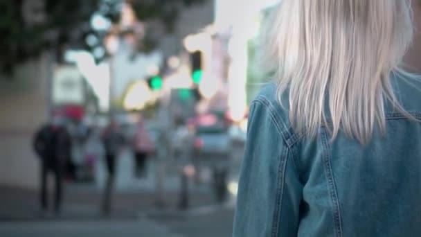 Vista trasera de la joven mujer con estilo en chaqueta de mezclilla caminando por el centro de la ciudad — Vídeos de Stock