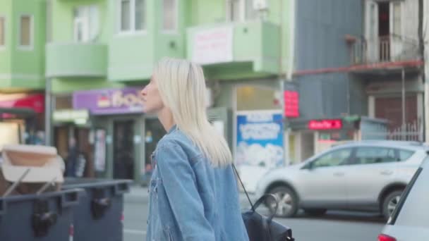 Vista posteriore di giovane donna elegante in giacca di jeans passeggiando per il centro della città — Video Stock