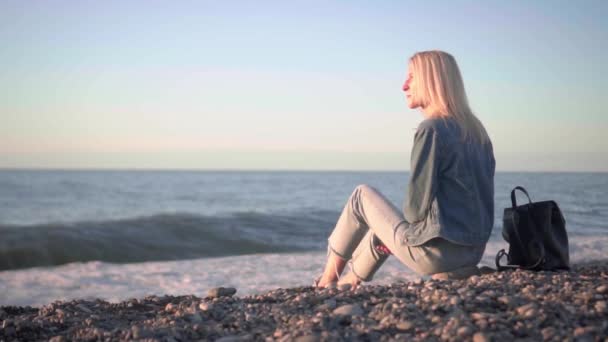 Flickan sitter vid havet och drömmer. Romantisk promenad längs vackra stranden. — Stockvideo