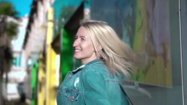 Zadní pohled na mladé stylové blondýny v džínové bundě procházky centrem města — Stock video