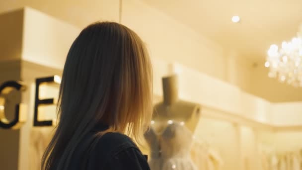 Flicka närmar sig fönstret i bröllopsbutiken och tittar på vackra brudklänningar — Stockvideo