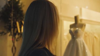 Kız gelinlik mağazasının vitrinine yaklaşır ve güzel gelinliklere bakar.