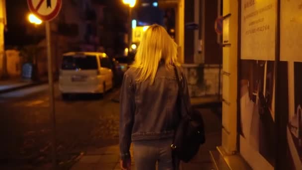 Bakifrån av ung elegant kvinna i denim jacka promenader genom stadens centrum — Stockvideo