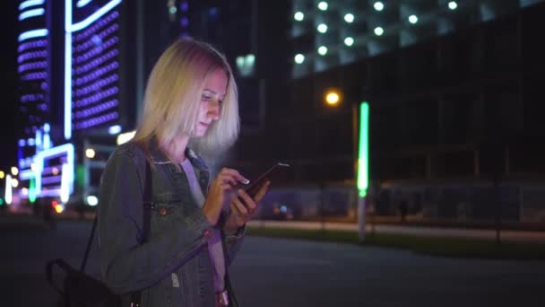 Kobieta używa smartfona do komunikacji w nocnym mieście. na tle drapaczy chmur — Wideo stockowe