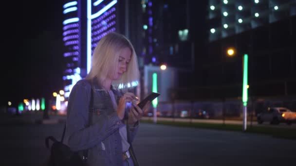 Γυναίκα χρησιμοποιεί smartphone για να επικοινωνούν στη νυχτερινή πόλη. με φόντο ουρανοξύστες — Αρχείο Βίντεο