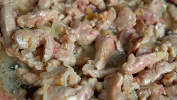 Stukken varkensvlees met gehakte uien tijdens het bakken in een oude koekenpan — Stockvideo