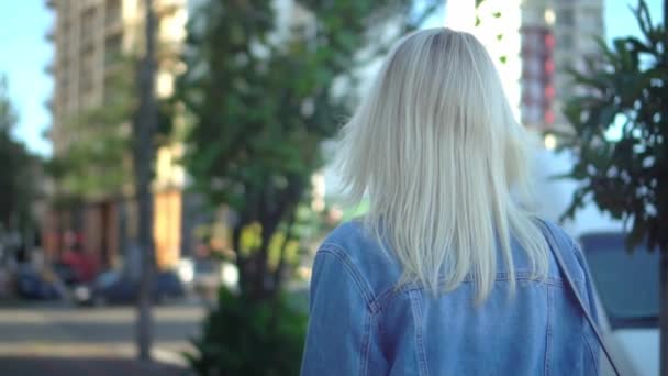 Vista trasera de la joven mujer con estilo en chaqueta de mezclilla caminando por el centro de la ciudad — Vídeos de Stock