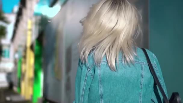 Οπίσθια όψη της νεαρής κομψής γυναίκας με τζιν σακάκι περπατώντας μέσα από το κέντρο της πόλης — Αρχείο Βίντεο