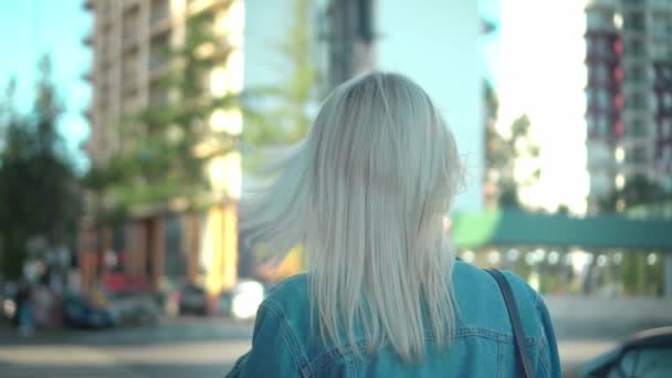 Bakifrån av ung snygg blond i denim jacka promenader genom centrum — Stockvideo