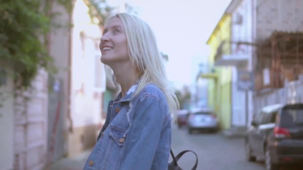 Rückansicht einer jungen, stylischen Blondine in Jeansjacke, die durch die Innenstadt läuft — Stockvideo