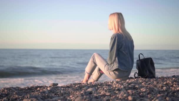 Chica está sentada junto al mar y soñando. Romántico paseo a lo largo de hermosa orilla. — Vídeo de stock