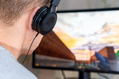 Kulaklıklı genç bir adamın evdeki bir bilgisayarda oyun oynaması.