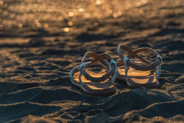 Gün batımında plajda üzerinde fotokopi alanı olan deri sandaletlerin yakın çekimi. Seyahat teması için güzel bir geçmiş, sahil tatili.