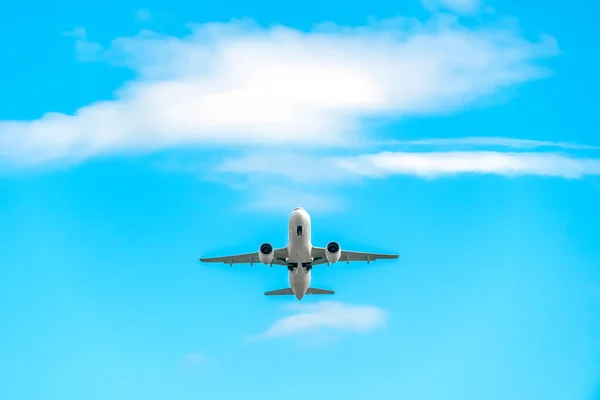Low-flying white passenger plane with landing gear on a background of blue sky with clouds with copy space, bottom view. Plane took off and hides the landing gear in flight