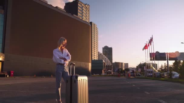 Bavullu kız şehrin arka planında duruyor, uzun gökdelenler. — Stok video