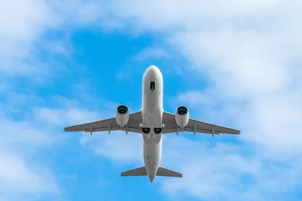 Close up low-flying white passenger plane with landing gear on a background of blue sky with clouds with copy space, bottom view. Plane took off and hides the landing gear in flight