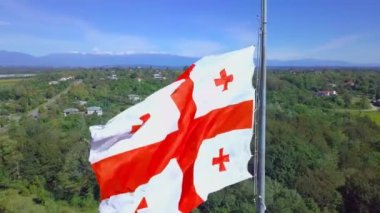 Gürcistan bayrağı arka planda karla kaplı yol köyünde dalgalanıyor.