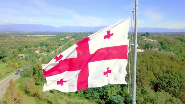 Bandeira georgiana está voando contra o fundo montanhas cobertas de neve estrada aldeia. — Vídeo de Stock