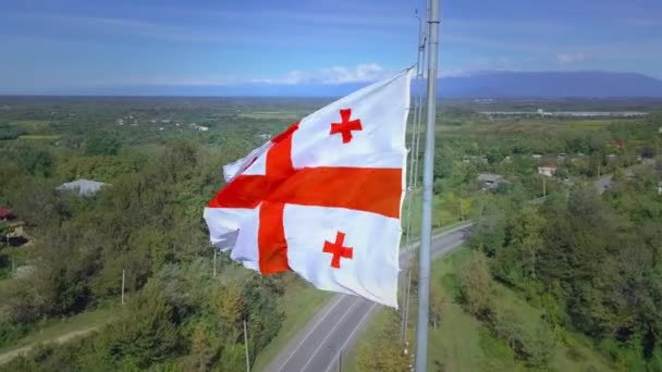グルジアの旗の背景雪に対して飛んでいる帽をかぶった山々の道路村. — ストック動画