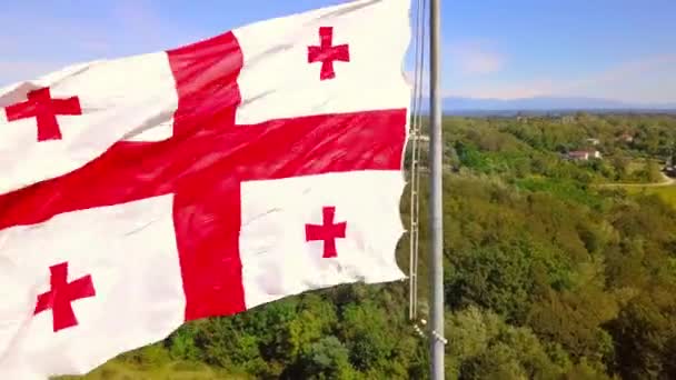Bandera de Georgia ondea contra el fondo nevado montañas pueblo de carretera. — Vídeos de Stock