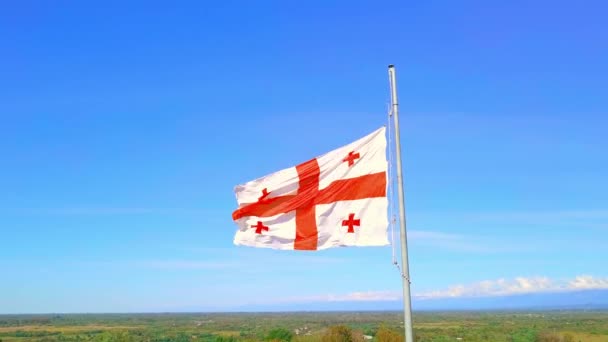 Georgian flag is flying against background snow-capped mountains road village. — Stock Video