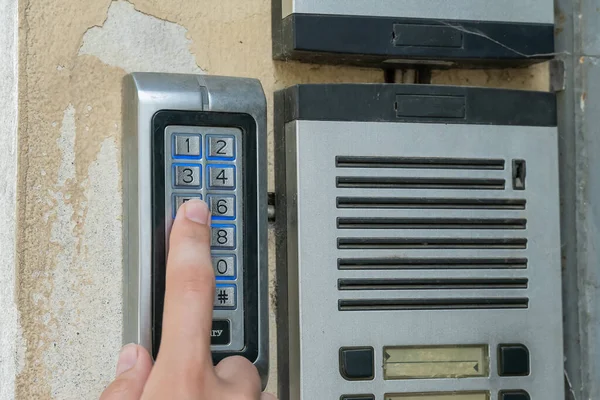 Kadının eli dahili telefondan bir düğmeye basıyor. Boş isim plakalı eski moda kapı zilleri. Boş isim kartları olan bir apartmanın dışındaki açık bir dahili telefon..