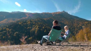 Erkekler ve kızlar katlanan koltuklarda oturup çay içip dağlara bakıyorlar.