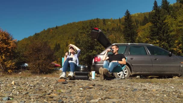 Mann und Mädchen sitzen auf Klappsitzen, trinken Tee und blicken auf die Berge — Stockvideo