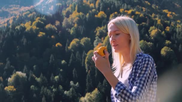 Une touriste femelle mange des kaki sur fond de montagnes. Camping. — Video