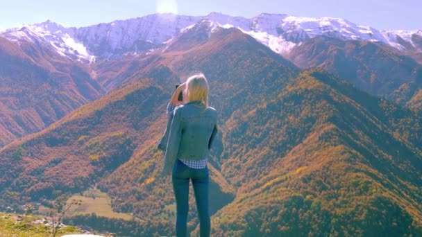 Hermosa rubia toma fotos o videos de un paisaje en las montañas de otoño. — Vídeos de Stock