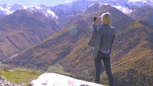 Hermosa rubia toma fotos o videos de un paisaje en las montañas de otoño. — Vídeos de Stock