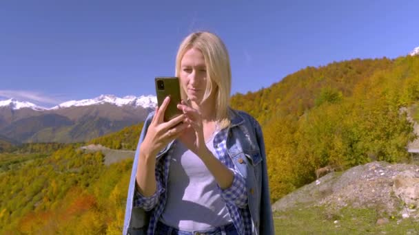 Όμορφη ξανθιά τραβά φωτογραφίες ή βίντεο από ένα τοπίο στα βουνά του φθινοπώρου. — Αρχείο Βίντεο