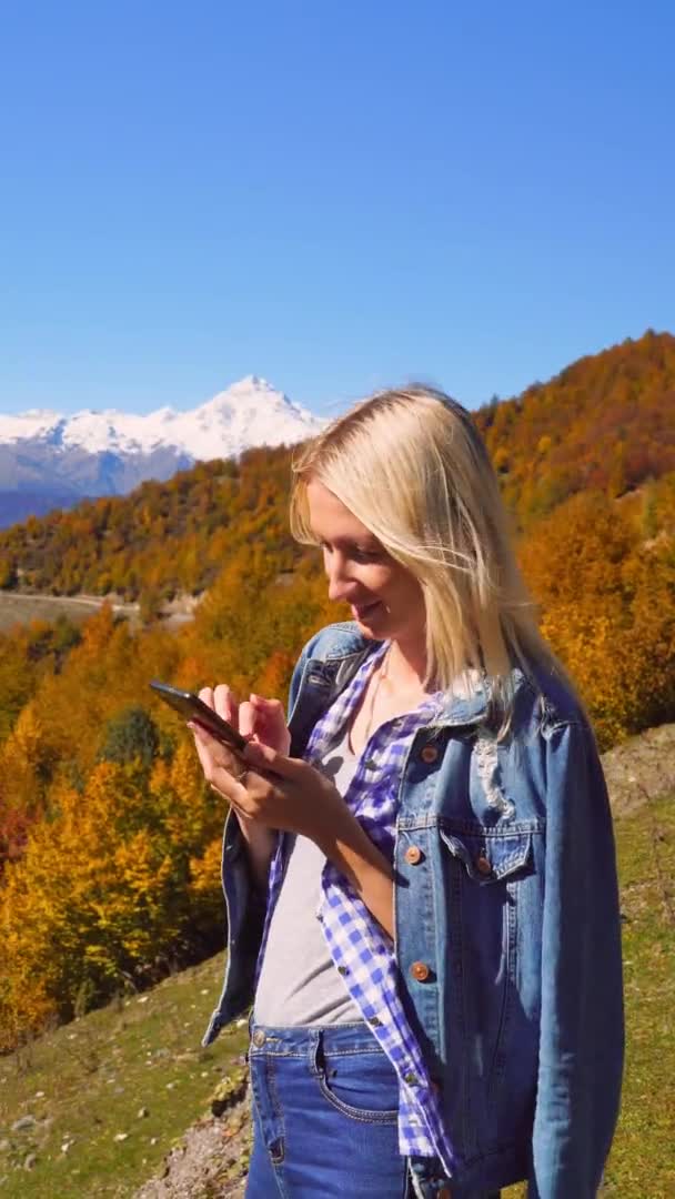 Belle blonde prend des photos ou des vidéos d'un paysage dans les montagnes d'automne. — Video