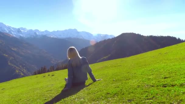 Une femme est assise dans un pré et profite de la vue sur les montagnes. — Video