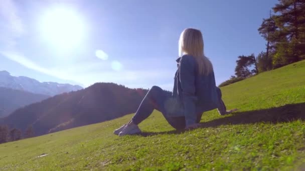 女性が牧草地に座って山の景色を楽しんでいます. — ストック動画