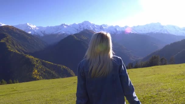 En kvinna sitter på en äng och njuter av utsikten över bergen. — Stockvideo