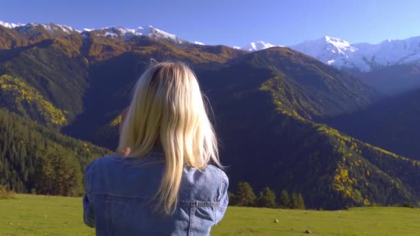 O femeie stă pe o pajişte şi se bucură de priveliştea munţilor.. — Videoclip de stoc