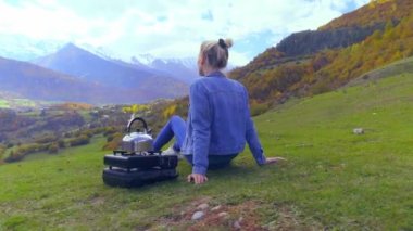 Bir kadın dağlara hayran, bir çaydanlık kaynıyor. Georgia.