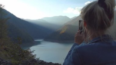 Güzel sarışın, sonbahar dağlarındaki bir manzaranın fotoğraflarını ya da videolarını çeker..