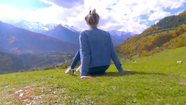 Eine Frau bewundert die Berge, neben ihr ein Metallbecher mit Tee oder Kaffee. — Stockvideo