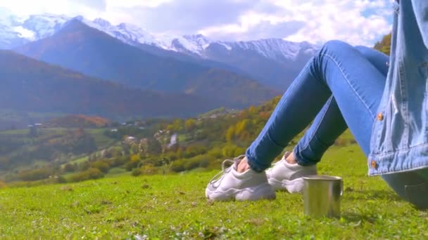 Una donna ammira le montagne, accanto a lei una tazza di metallo con tè o caffè. — Video Stock